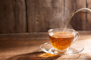 Pour hot tea into a teacup. A cup of herbal tea placed on an old wooden table, dark background. A...