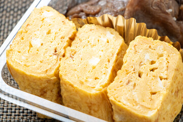 お弁当に入れられた卵焼きのアップ。弁当容器は使い捨ての透明プラスチックパック。
