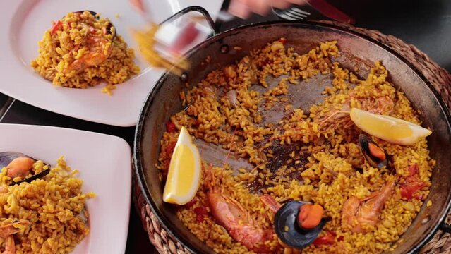 Pan of just cooked paella de marisco served on table in restaurant with pieces of lemon and spoons.