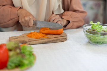 healthy food, weight loss concept beautiful asian muslim woman Attractive woman in headscarf prepares delicious food at kitchen, chopping carrots to nourish skin health care concept