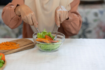 Obraz na płótnie Canvas Young Muslim woman in hijab eats vegetable salad healthy food in the kitchen Fasting concept, vegetarian diet, vegan diet