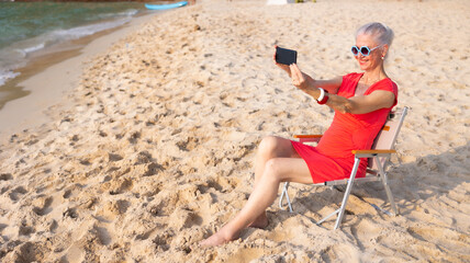 Selfie. Elderly caucasian female taking selfie with smartphone on beach. Vacation trip summer holiday.