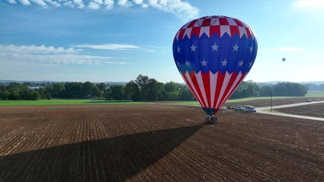 Aerial approaching shot of american hot air balloon landing on agricultural field during sunny day with blue sky