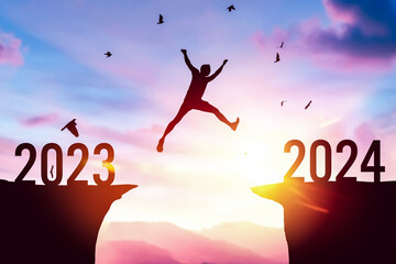 Silhouette man jumping between cliff with number 2023 to 2024 and birds flying at top of mountain background. Freedom challenge and travel adventure holiday concept.