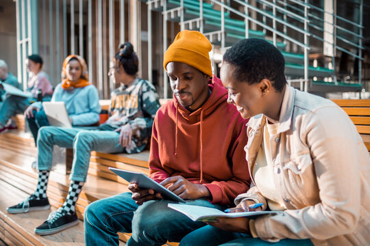 Two young friends studying and using a tablet in a lobby of a college or university library