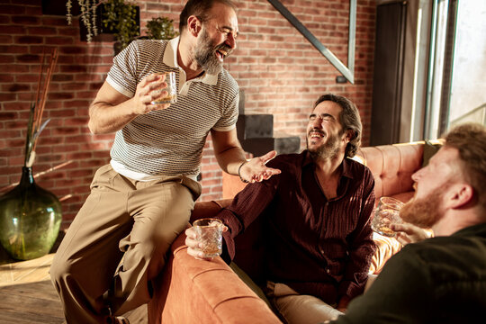 Male friends drinking whiskey and telling stories at home in the living room