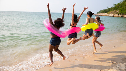 Jumping. Group of teenager girls jump on the beach. Four teenager girl female enjoying on inflatable ring and dance on tropical beach. Vacation trip summer holiday. Gen Z