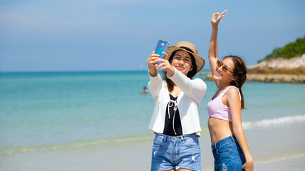 Selfie on the beach. Two friens teenager girl woman holding smart phone in hand shooting selfie photo on tropical beach. Vacation trip summer holiday.