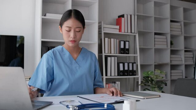 Asian female medical student studies a medical textbook on a laptop computer in a hospital hall.