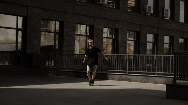 Electro dance performed by an athlete. Handsome young hipster man in a black T-shirt and jeans posing in an urban setting.