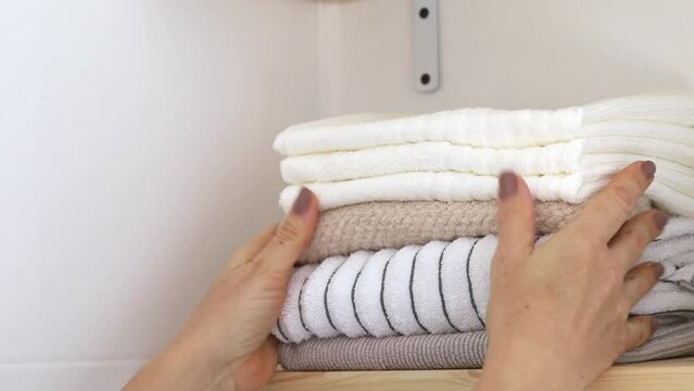Close-up woman's hands stack clean towels on a shelf.