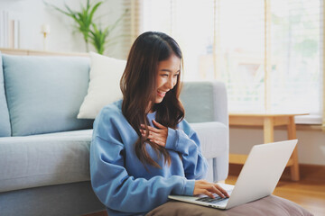 Young asian woman smile working in living room at home. Happy female using computer laptop and...