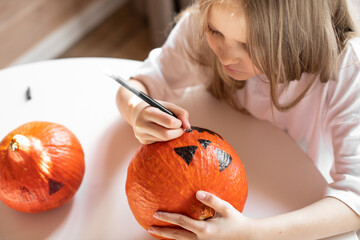 Girl draws on a pumpkin, preparing for Halloween