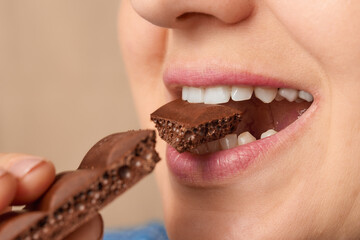 Close up of the mouth of a Caucasian woman biting off a piece of porous chocolate. Three-quarter...