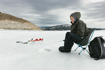 Frozen lake with a boy ice fishing in hole in snow in winter