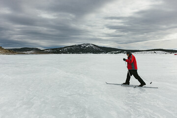 Man cross country skies across frozen lake in mountains