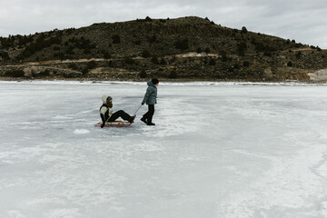 Fototapeta na wymiar Boy pulls his grandma on sled across a frozen lake in winter
