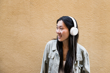 Young happy woman listening music with headphones standing outside.