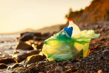Close up of plastic green bag full of trash lies on pebble wild coast. Copy space. Concept of...