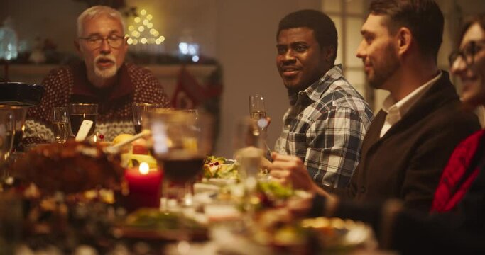 Portrait of a Handsome Young Black Man Proposing a Toast at a Christmas Dinner Table. Family and Friends Sharing Meals, Raising Glasses with Champagne, Toasting, Celebrating a Winter Holiday