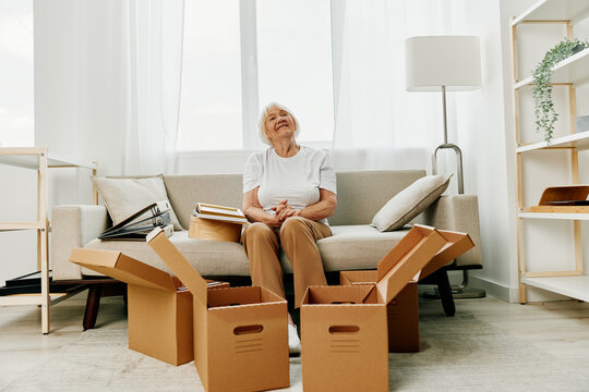 an elderly woman sits on a sofa at home with boxes. collecting things with memories and moving.