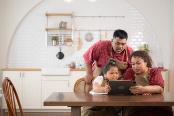A plus-size family with a father wearing a prosthetic leg, is happily assisting a child with her homework and having fun together in the dining room of the house before cooking together