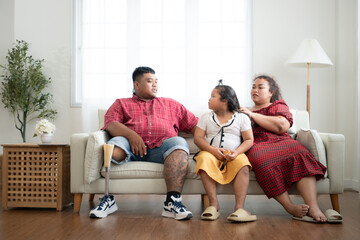Obraz premium A plus size family with a father wearing a prosthetic leg, Resting and talking with daughter on the weekly holiday, in the living room of the house.