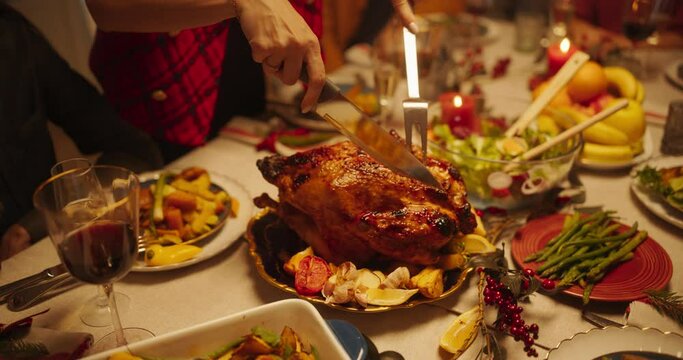 Festive Thanksgiving Dinner or Christmas Celebration Family Meal. People Sitting Behind a Dining Table while a Young Female Carving a Turkey Feast with Baked Potatoes. Close Up Zoom Out Footage