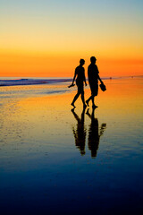 Obraz premium Young couple walking at edge of sea on romantic sunset beach.