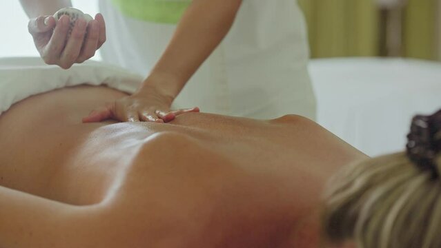 Hot cowrie sea shell relaxing back rub on caucasian woman's, Maldives