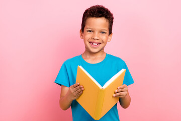 Photo of cheerful positive little boy dressed blue t-shirt reading interesting book isolated pink color background