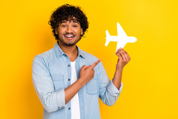 Photo of handsome man with curly hairdo dressed denim shirt indicating at paper white plane in hand isolated on yellow color background