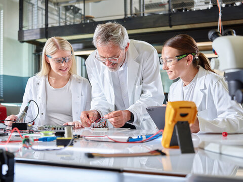 Professor teaching trainees with circuit board in laboratory