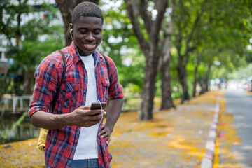 Smiling young man wearing in-ear headphones listening to music and using smart phone