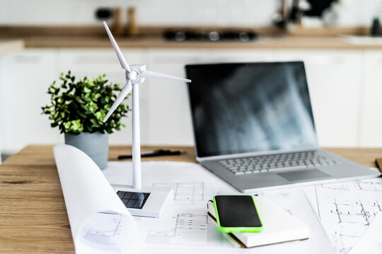 Wind turbine model, construction plan, cell phone and laptop on table in office