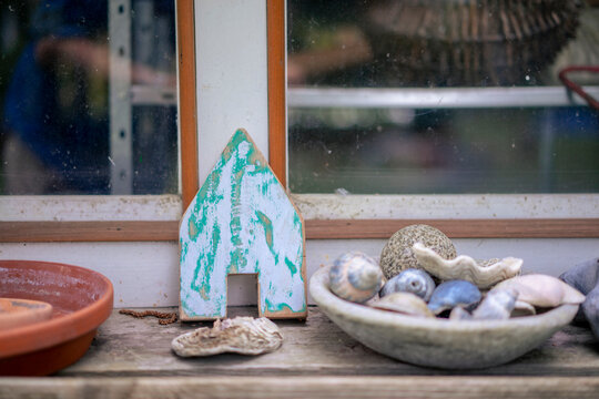 Various sea shells in bowl with model house on table near window