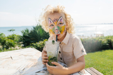 Girl with face painting drinking mojito in garden on sunny day