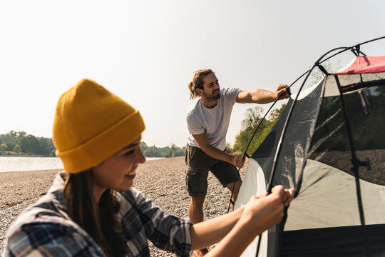 Smiling young couple setting up a tent at the riverside