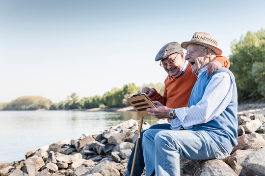 Two old friends sitting by the riverside, using digital tablet