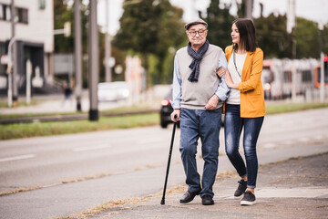 Adult granddaughter assisting her grandfather strolling with walking stick