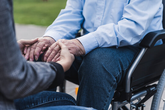 Young woman holding hands of senior man sitting in wheel chair, partial view