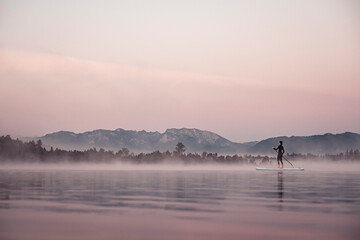 Woman stand up paddling on lake Kirchsee at morning mist, Bad Toelz, Bavaria, Germany