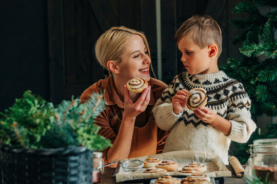 Smiling mother and son holding cinnamon buns at table