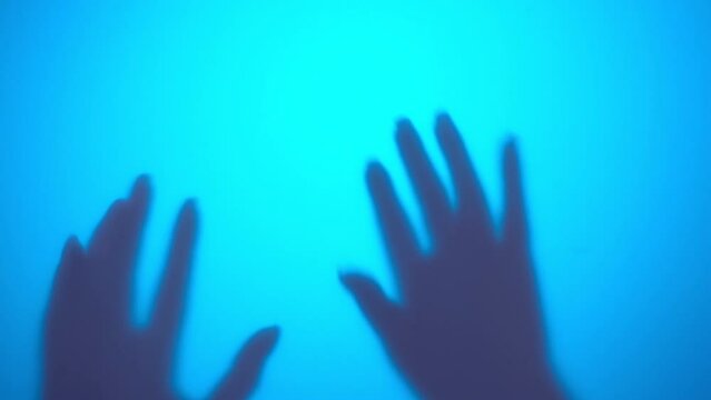 Dreadful video of hands of woman touching blue background with quick slams, contacting illuminated by contour light wall with fingers attempting to grab and scary, creating scene of fear.