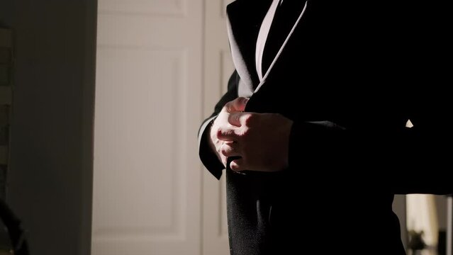 Silhouette Of A Man Putting On His Jacket In Dark Room On The Background Of The Window. Close Up Shot Footage