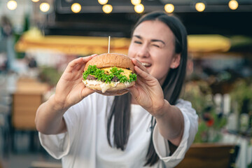 A young woman eating burger in street cafe.