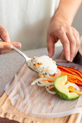 Woman preparing spring rolls in rice paper on kitchen table.