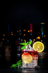 Bramble cocktail drink with dry gin, liqueur, syrup, lemon juice, blackberry, mint and ice. Black...