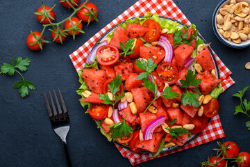 Gourmet salad with sweet juicy watermelon, cherry tomatoes, red onion, peanuts and parsley, black table background, top view