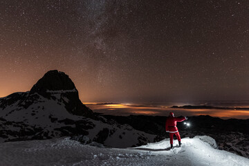 Night landscape with Santa Claus holding lantern in snowy mountains during Christmas time
